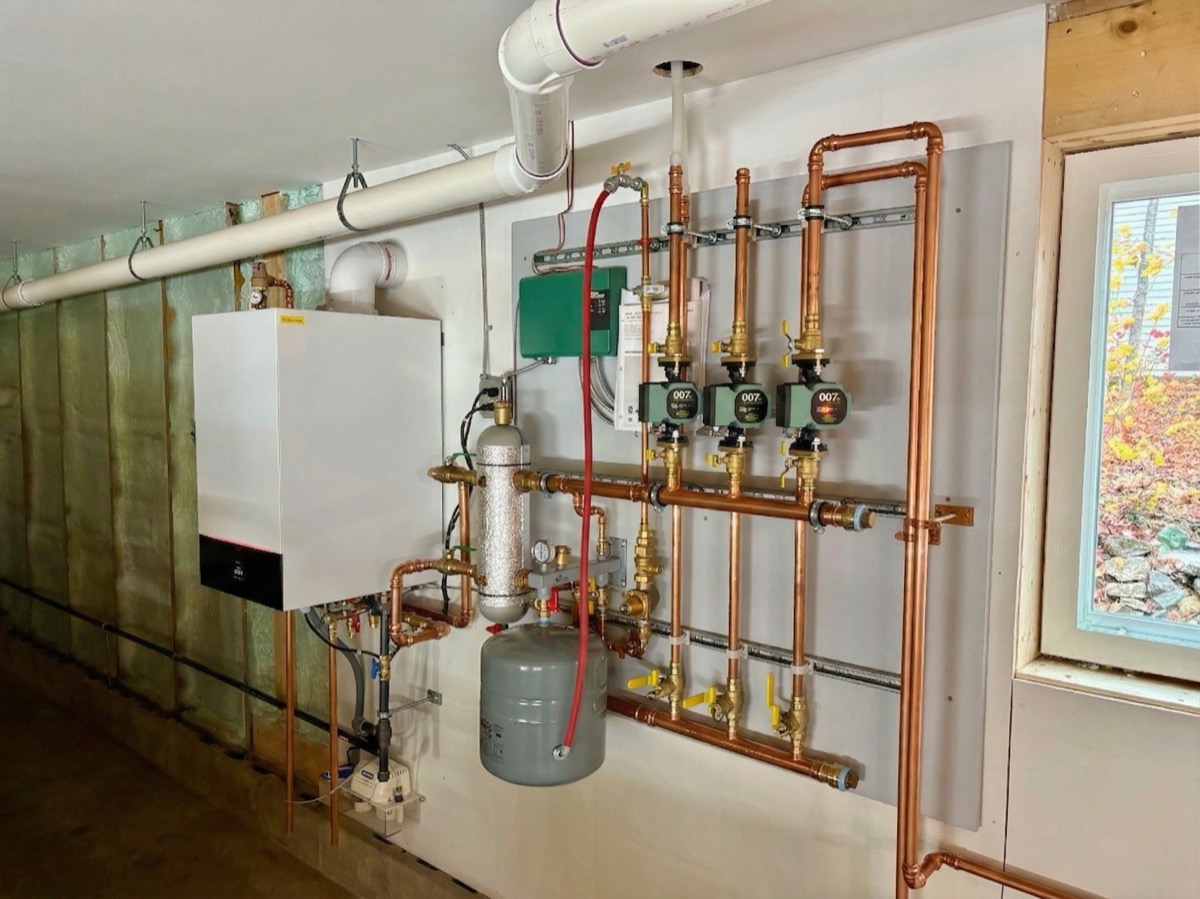 Technician installing a wall-hung condensing boiler in a Maine home basement