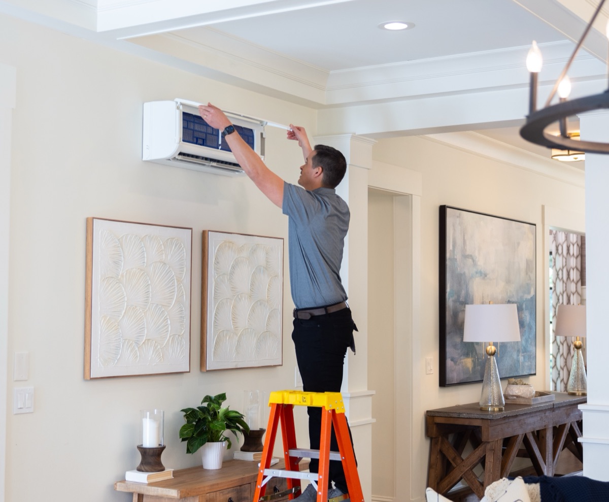 Technician installing a Mitsubishi mini-split heat pump head unit in a Maine living room